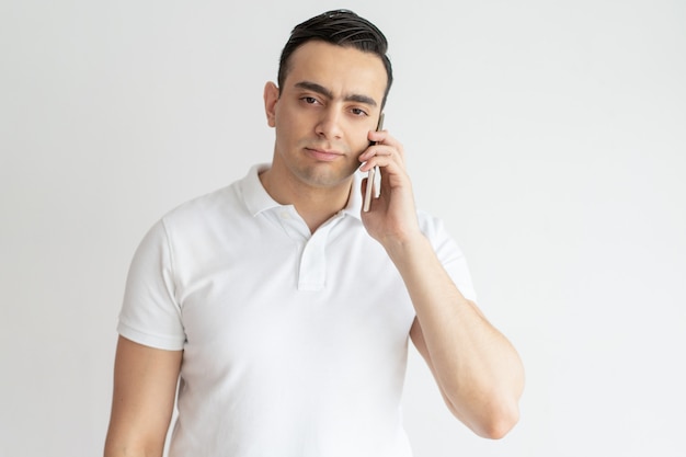 Serious young man talking on smartphone and looking at camera