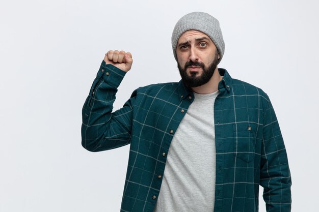 Free photo serious young man wearing winter hat looking at camera showing knocking gesture isolated on white background