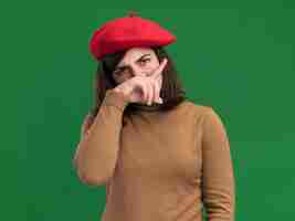 Free photo serious young pretty caucasian girl with beret hat puts hand on nose isolated on green wall with copy space