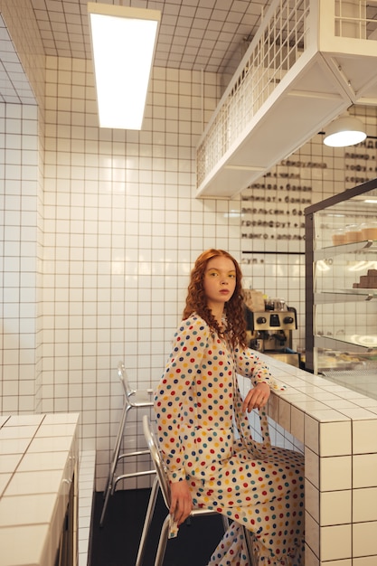 Free photo serious young redhead curly lady sitting in cafe.