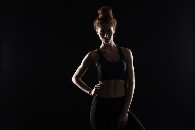 Serious young sports lady standing over black wall