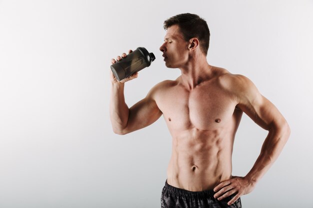 Serious young sportsman drinking water