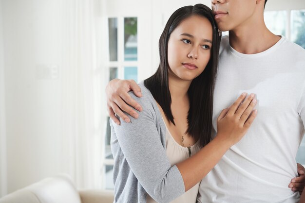 Serious young woman deep in thoughts hugging her boyfriend
