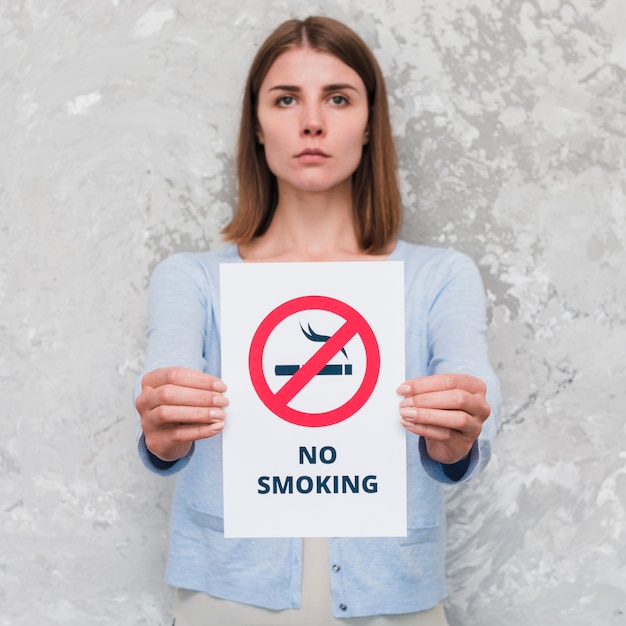 Free photo serious young woman holding social message paper of no smoking