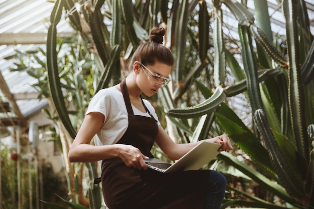 Serious young woman sitting in greenhouse using laptop