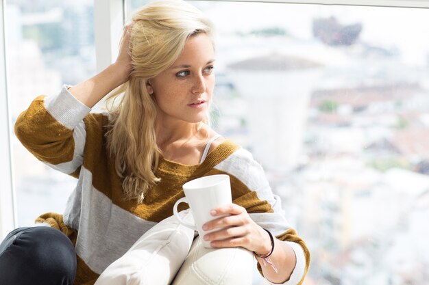 Серьезная молодая женщина, сидя у себя дома с чашкой чая
