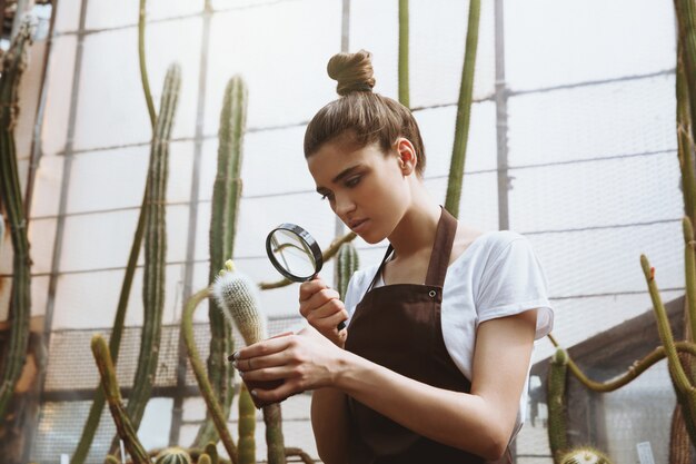 Serious young woman standing in greenhouse near plants