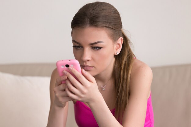 Serious young woman using cellphone at home