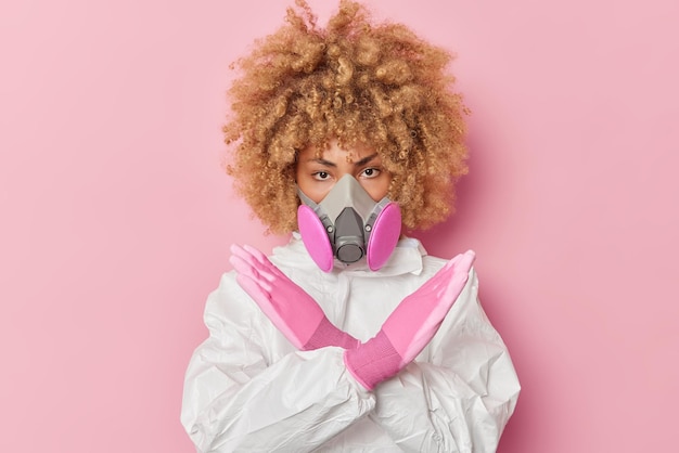 深刻な若い女性は化学防護服を着ており、呼吸器は停止ジェスチャータブーサインを入れないようにしますピンクの背景に隔離された危険を防ぐために試みますバイオハザードの概念