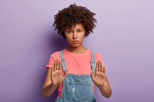 オーバーオールでポーズをとるアフロの真面目な若い女性