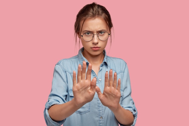 Serious young woman with glasses posing against the pink wall