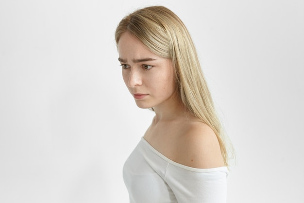 serious young woman with straight hair posing isolated, frowning, having absent-minded facial expression, thinking over some problem. Nervousness and uneasiness