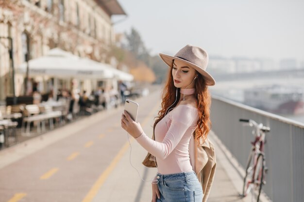 Serious young woman with wavy ginger hair making selfie