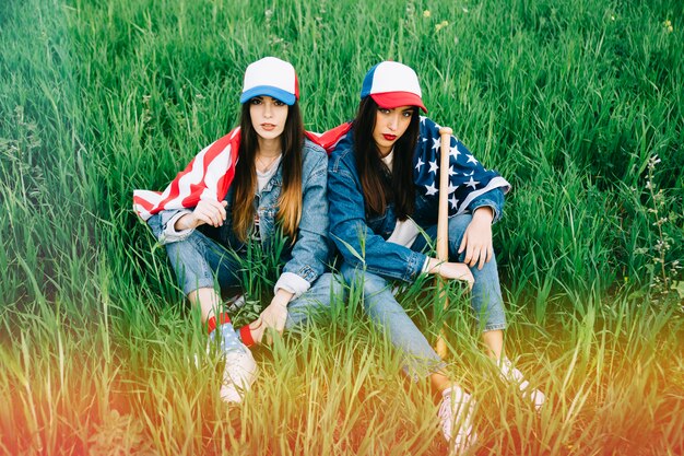 Serious young women with American flag sitting on grass