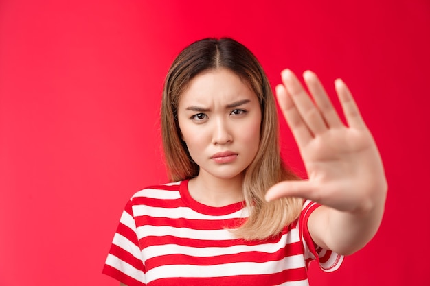 Seriouslooking alarmed angry asian woman pull hand forward stop no sign demanding and prohibiting be...