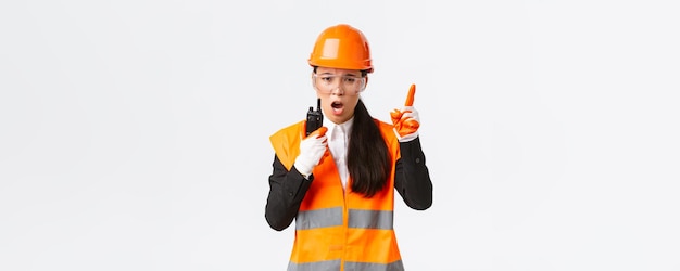 Tecnico di ingegnere industriale femminile asiatico serio in casco di sicurezza e contro di comando uniforme