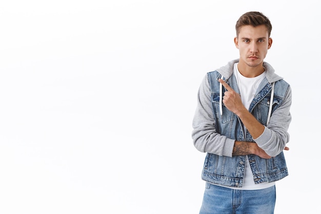 Seriouslooking confident young slim tall guy with blond hair look camera concentrated assured pointing finger at upper left corner as showing best deal standing white background