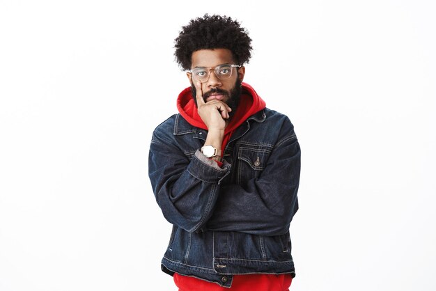 Seriouslooking throughtful goodlooking africanamerican hiphop dancer with beard in glasses and denim jacket over hoodie touching face with finger