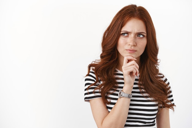 Free photo seriouslooking young redhead woman scheming something look suspicious and hesitant having doubts express trong disbelief as pondering information touch chin frowning look sideways thoughtful