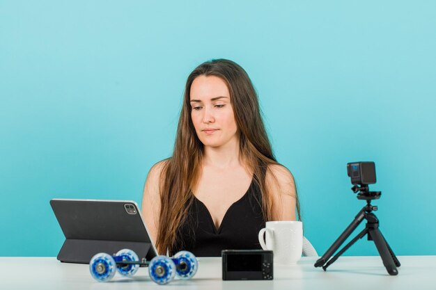 Seriously blogger girl is looking at tablet screen on blue background