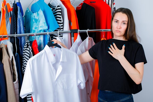 Seriously girl is holding shirt and putting other hand on chest on clothes background