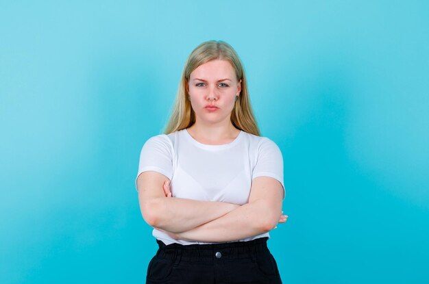 Seriously girl is looking at camera by crossing arms on blue background
