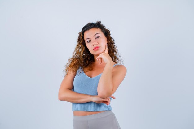 Seriously girl is looking at camera by holding forefinger on cheek on white background