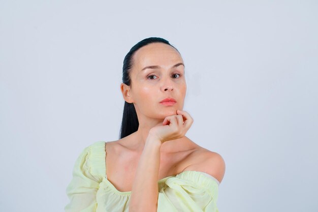 Seriously girl is looking at camera by holding hand under chin on white background