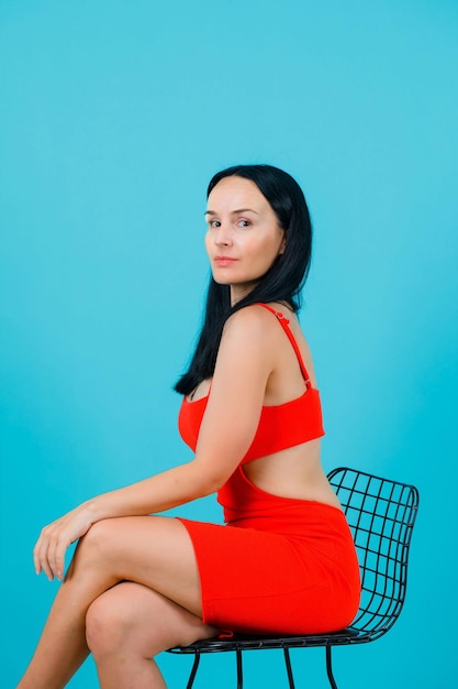 Free photo seriously girl is looking at camera by putting arm on knee on blue background