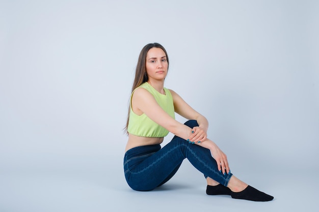 Seriously girl is looking at camera by sitting on floor on white background