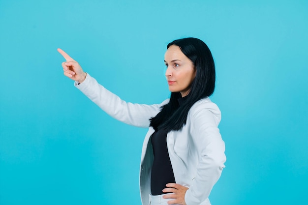 Seriously girl is pointing left up with forefinger on blue background