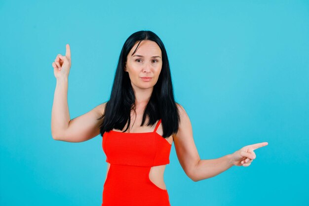 Seriously girl is pointing up and right with forefingers on blue background