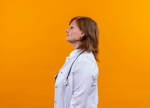 真剣に探している中年女性医師医療ローブとコピースペースと孤立したオレンジ色の壁に縦断ビューで聴診器立って身に着けています。