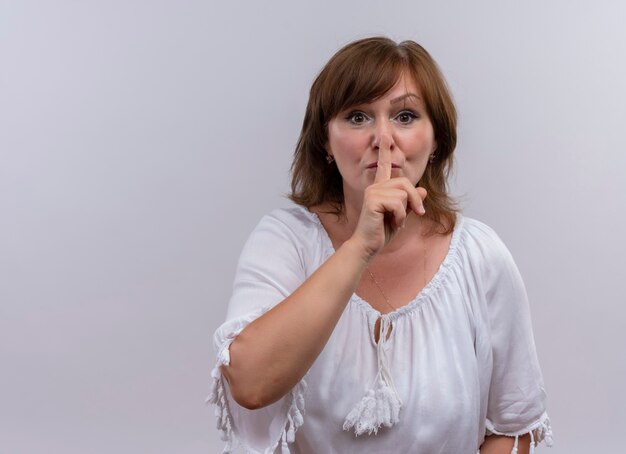 Серьезно выглядящая женщина средних лет, закрыв рукой губу, жестикулируя молчанием на изолированной белой стене