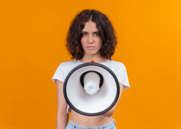 Free photo seriously looking young beautiful woman holding speaker on isolated orange wall with copy space