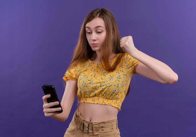 Seriously looking young girl holding mobile phone and raising fist on isolated purple space