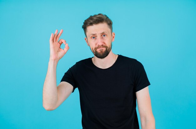 Seriously man is hsowing okay gesture by raising up his hand on blue background