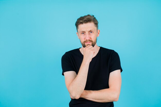 Seriously man is looking at camera by putting hand on chin on blue background