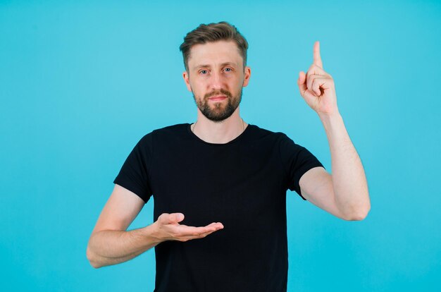 Seriously man is pointing up with forefinger on blue background