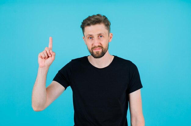 Seriously man is pointing up with forefinger on blue background