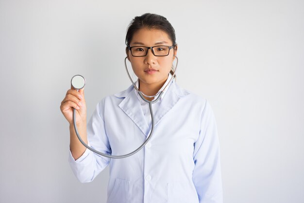 Serous young asian female doctor using stethoscope. medical testing concept.