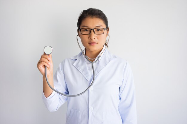 Serous若いアジアの女性の医者は、聴診器を使用しています。医療検査のコンセプト。