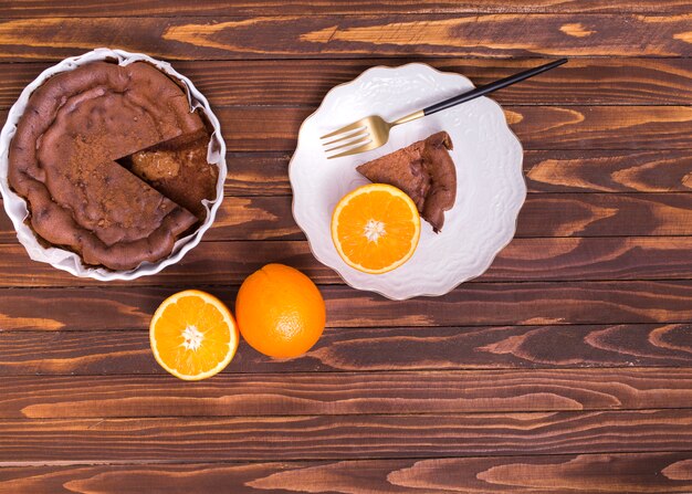 Served cake slice and halved citrus fruit on white ceramic plate against wooden table