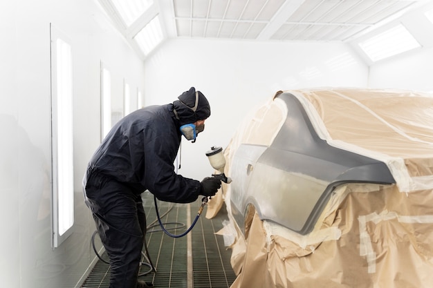 Service worker painting car in auto service