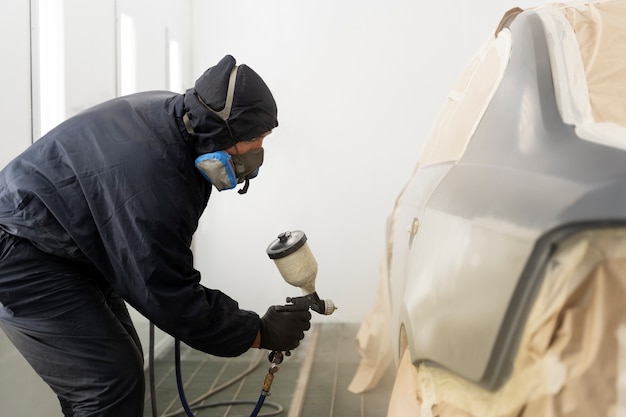 Service worker painting car in auto service