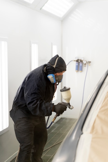 Service worker painting car in auto service