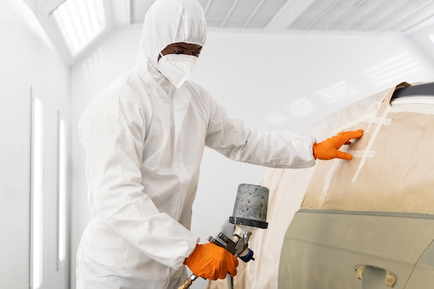 Service worker painting car in auto service