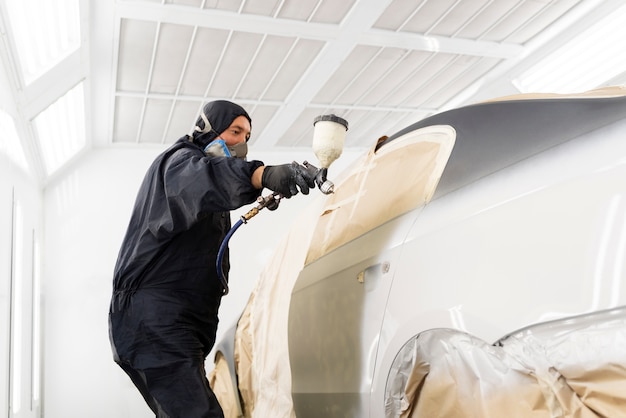 Service worker painting car in auto service