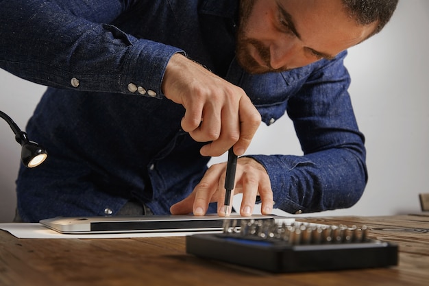 Serviceman uses screwdriver to close backside topcase of personal computer laptop after repairing and cleaning service in his lab