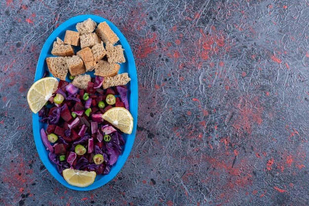 Serving of beet and red cabbage salad with dried crust and lemon slice garnish on dark colored background. High quality photo